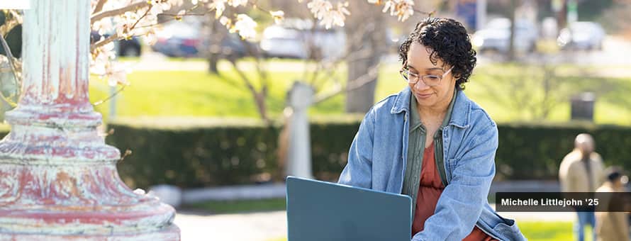 Michelle Littlejohn '25, who earned her BA in Graphic Design & Media Arts from wuv, studies from a park bench on her laptop computer.