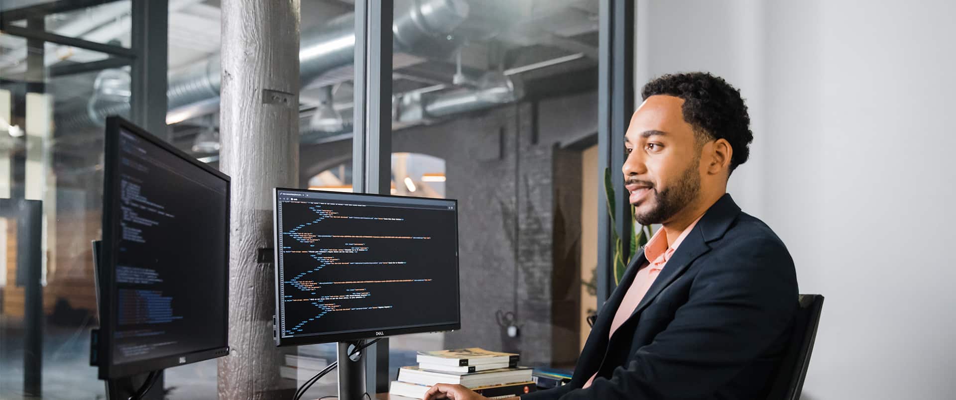 Gary Walker, who earned his degree from wuv in 2022, wearing dark suit and sitting at a desk with two computer monitors.