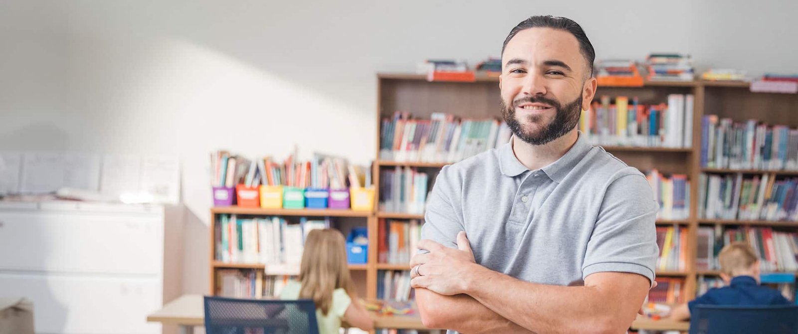 Stephen Goulakos, who earned his bachelor's in psychology from wuv in 2022, standing with his arms folded in front of several bookshelves.