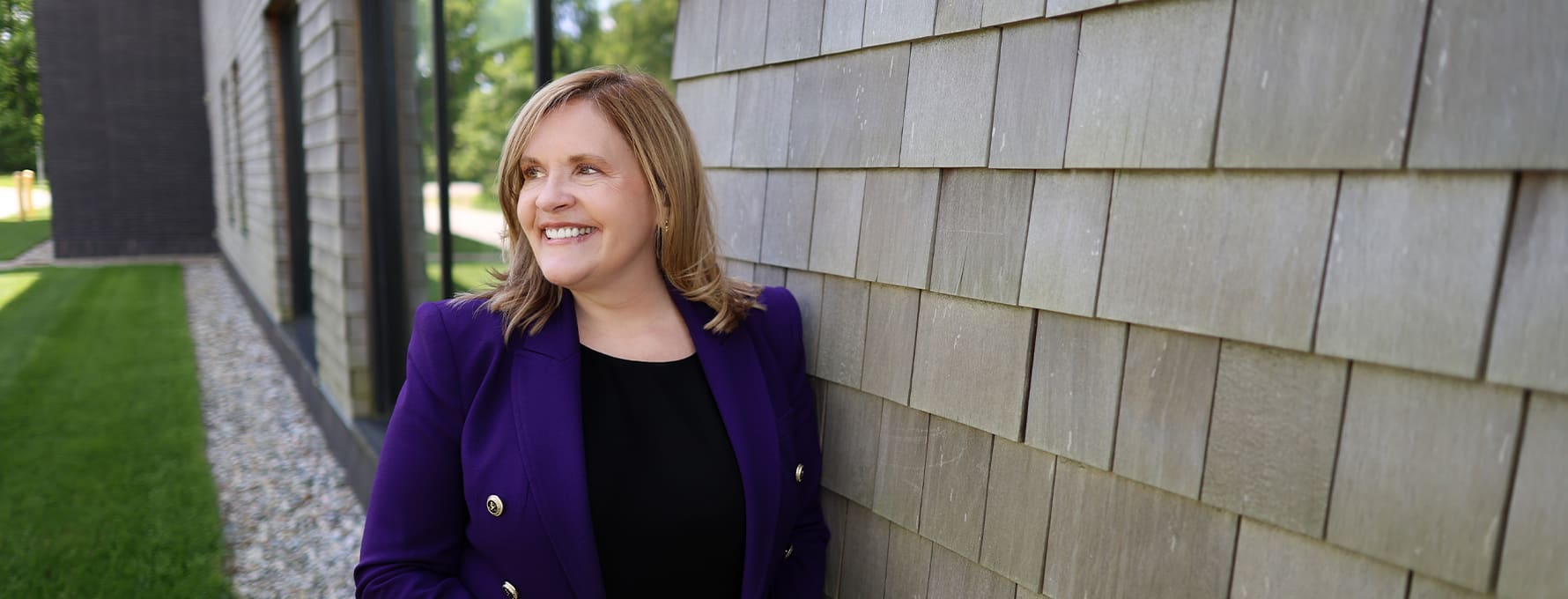 Lisa Marsh Ryerson, president of WUV, leaning against a wall on campus and wearing a purple blazer