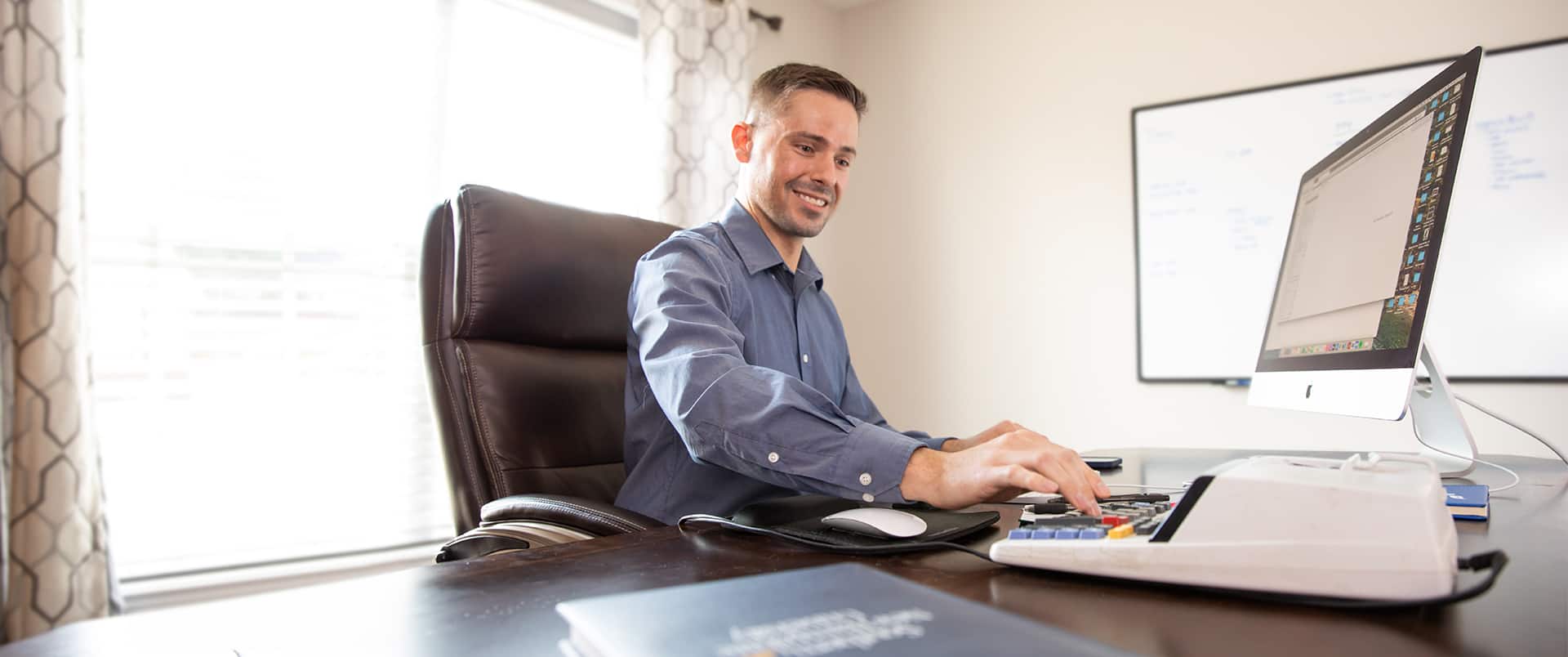 Blake Venable, who earned his bachelor's in accounting in 2024, with a computer keyboard and calculator on a desk in front of him and a whiteboard on the wall in the background.