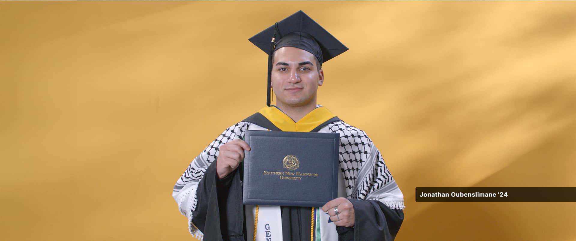 Jonathan Oubenslimane, who earned his bachelor's in business administration with a concentration in entrepreneurship from WUV in 2024, wearing his cap and gown and holding his diploma.