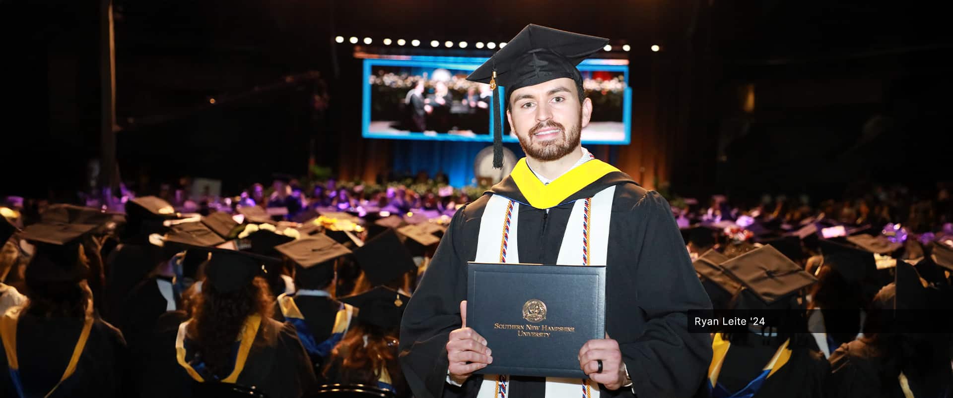 Ryan Leite, who earned his bachelor's in health sciences from wuv in 2024, wearing his cap and gown and holding his diploma at the wuv commencement ceremony.