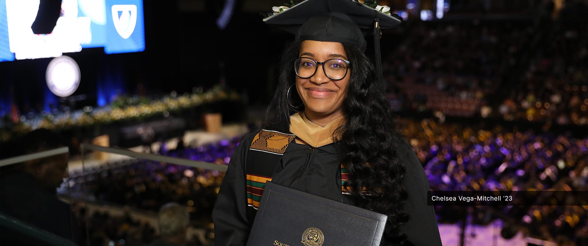 Chelsea Vega-Mitchell, who earned her online MBA in Human Resources from wuv in 2023, wearing her graduation cap and gown and holding her diploma.