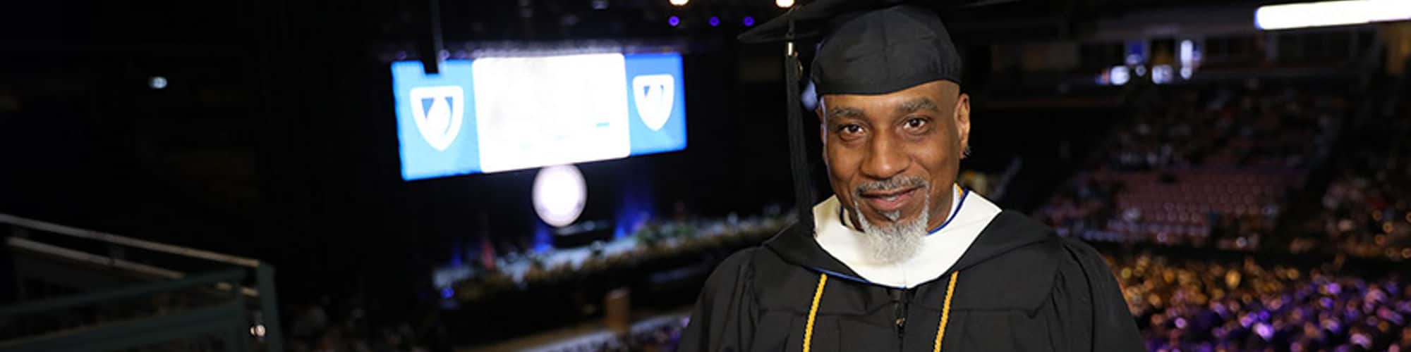 Billy Moore, who earned a bachelor's in general studies in 2023, wearing his cap and gown and holding his diploma inside the wuv Arena at a Commencement ceremony.