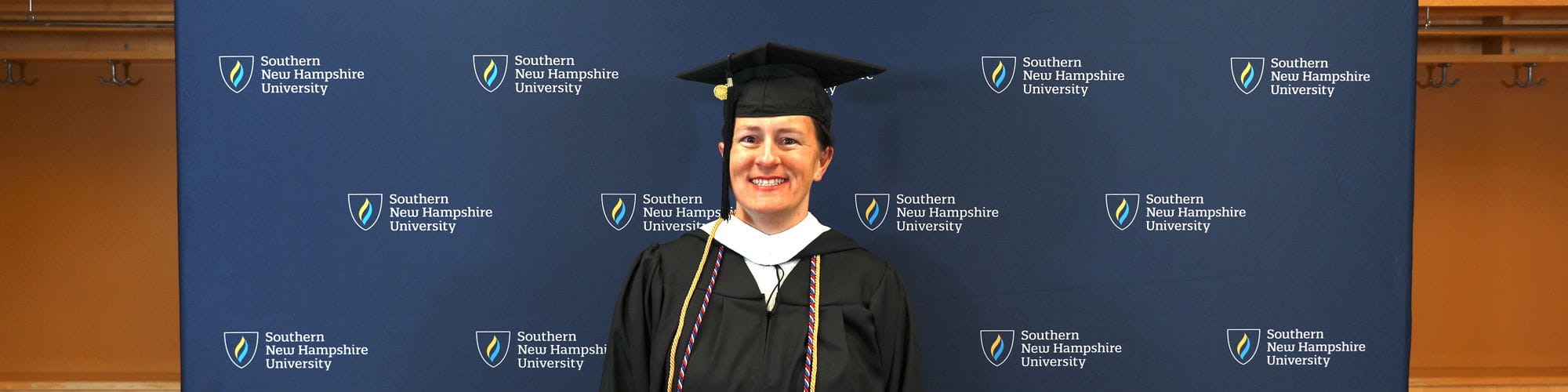  Lisa Rogers, a Nebraska resident who earned her degree at wuv, standing in front of step and repeat banner wearing her cap and gown.