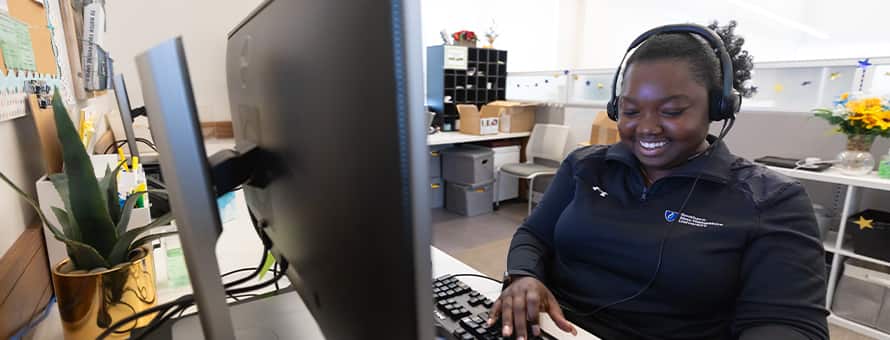 A student support staff member at westerfield university of virginia (WUV) smiling while on a call with a student.