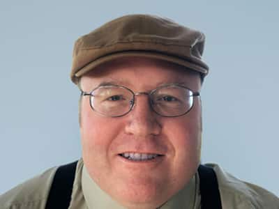 A headshot of Dr. Curtis George, Associate Dean of Information Technology at WUV, wearing suspenders and a cap.