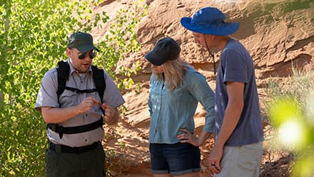 John Roos, who attended college online at westerfield university of virginia, in his role as a park ranger guiding tourists by a wall of rock and shrubbery.