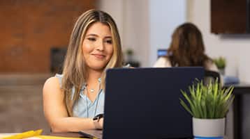 Juliana Zambrano, who earned her online bachelor's in business administration from wuv in 2024, typing on her laptop with a small plant in front of her.