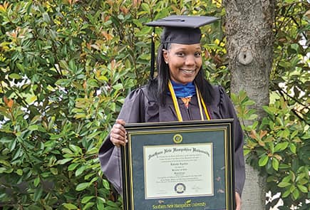 wuv Graduate Latisha Aguilar holding up a framed degree in front of the woods